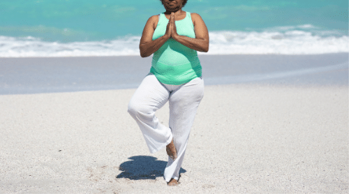 older woman doing yoga on the beach featured