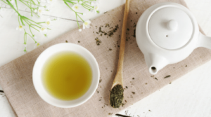 green tea in cup with spoon of tea leaves and teapot featured