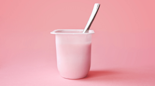 yogurt cup with spoon on pink background featured