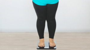 overweight woman in black and blue leggings standing on scale featured
