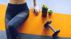 woman on orange yoga mat with dumbbell, apple and shaker featured