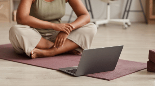 woman starting online yoga program sitting on yoga mat with laptop featured