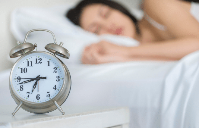 woman sleeping in background, alarm clock in front