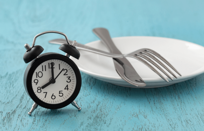 clock and empty plate with knife and fork, intermittent fasting
