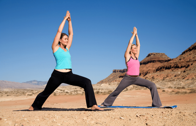 Two women doing Warrior I yoga pose in the desert