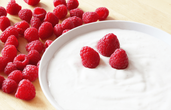Bowl of greek yogurt with raspberries around it, and three berries on top of the yogurt