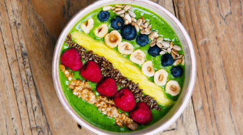 Smoothie Bowls Featured - Green smoothie bowl with fruit and nuts and etc. on top in lines.