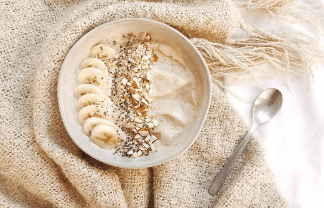 Light tan smoothie bowl with banana slices, seeds and other toppings. 