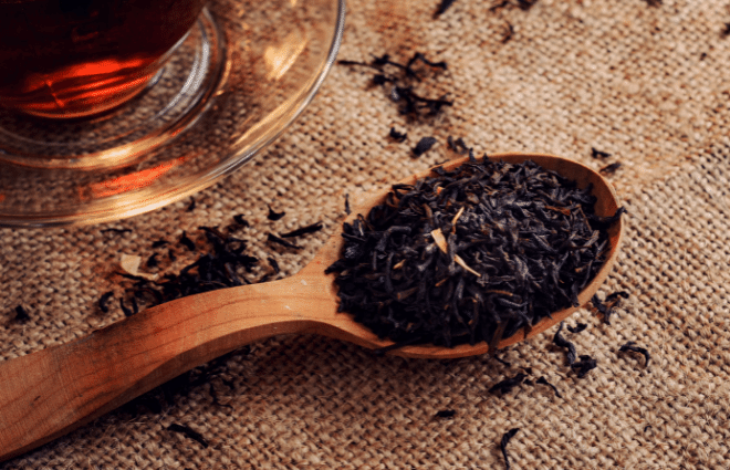 Black tea leaves in a wooden spoon with a glass of tea