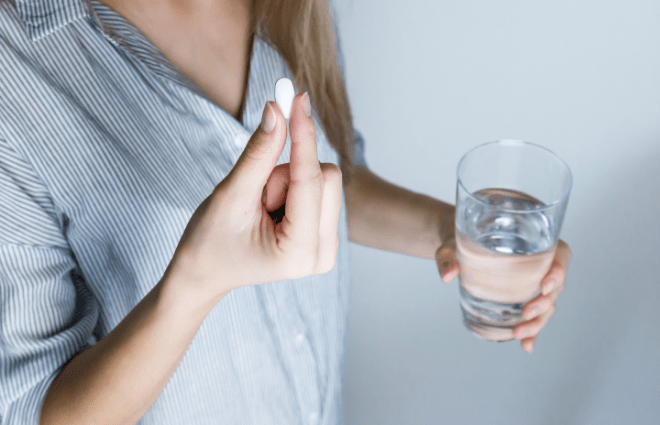 Woman taking vitamins with a glass of water