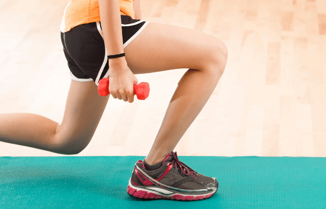 Woman doing a lunge on a green yoga mat holding a very small hand weight