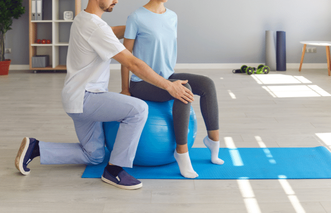 Physical therapist helping a woman perform an exercise on a yoga ball 
