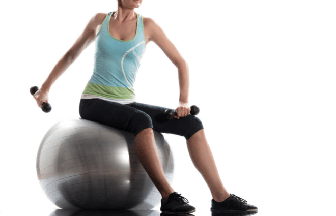 Woman sitting on a yoga ball working out with small hand weights