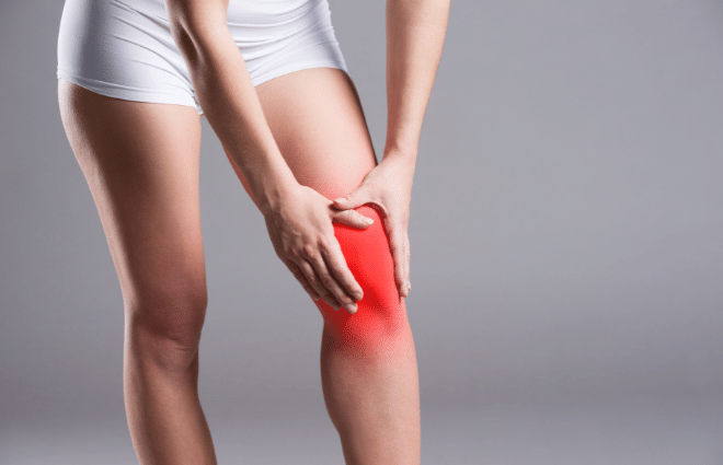 Woman in white shorts holding knee that is highlighted red to indicate knee pain
